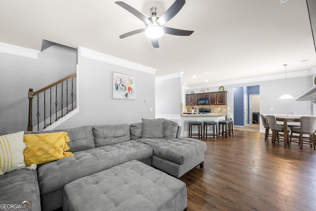 living area with ceiling fan, stairs, ornamental molding, and dark wood finished floors
