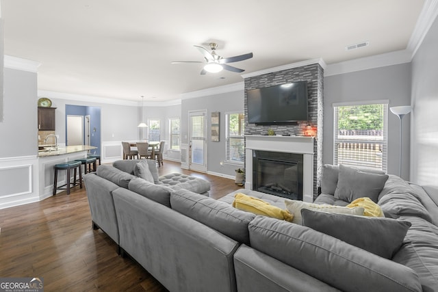 living room featuring ornamental molding, dark wood-style floors, a large fireplace, and ceiling fan