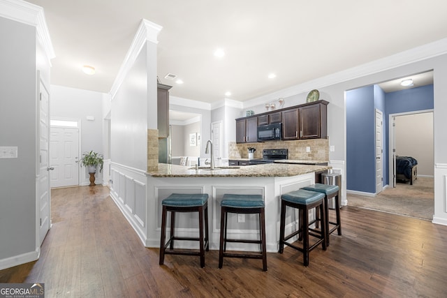 kitchen with a sink, dark brown cabinetry, light stone countertops, a breakfast bar, and black appliances