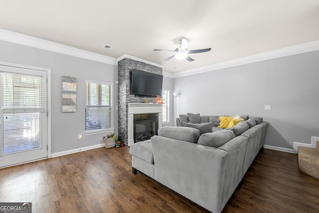 living area with dark wood-style flooring, crown molding, a large fireplace, and ceiling fan