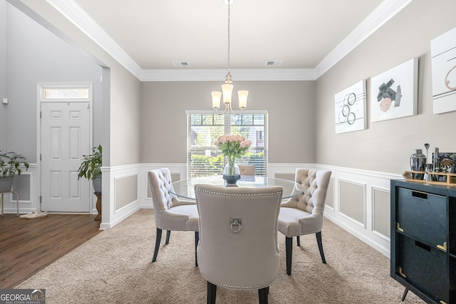 carpeted dining room featuring a decorative wall, a chandelier, a wainscoted wall, ornamental molding, and visible vents