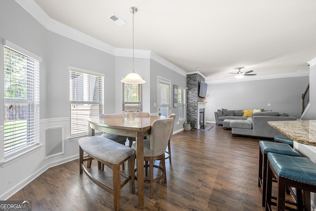 dining area with dark wood-style flooring, visible vents, a ceiling fan, a fireplace, and ornamental molding