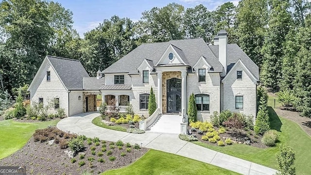 french country inspired facade featuring brick siding, stone siding, a chimney, and a front yard