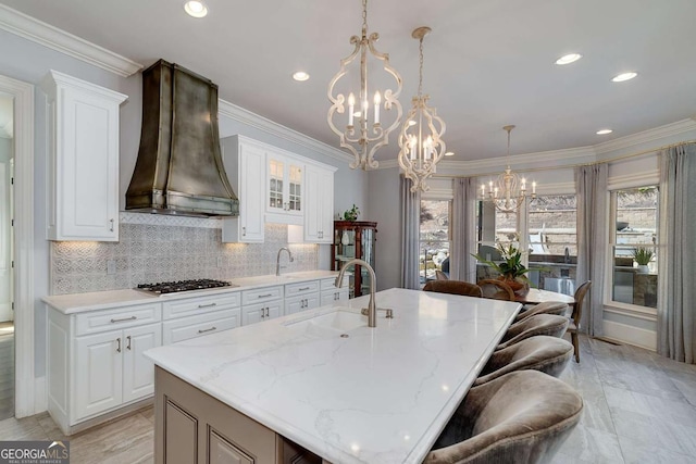 kitchen with backsplash, stainless steel gas cooktop, a sink, an inviting chandelier, and wall chimney exhaust hood