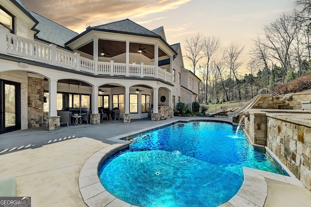 pool at dusk with a patio, a water slide, a ceiling fan, and an outdoor pool
