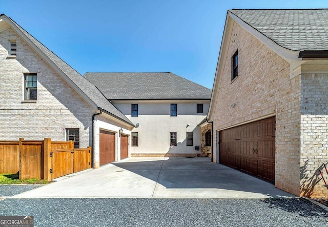 view of home's exterior with brick siding, a shingled roof, fence, and concrete driveway