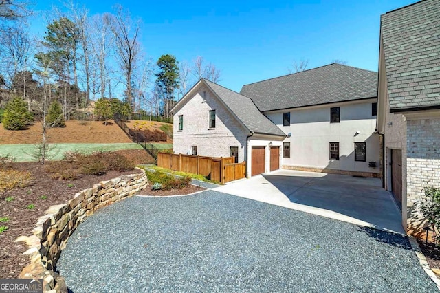 view of front of house with roof with shingles, an attached garage, brick siding, stucco siding, and driveway