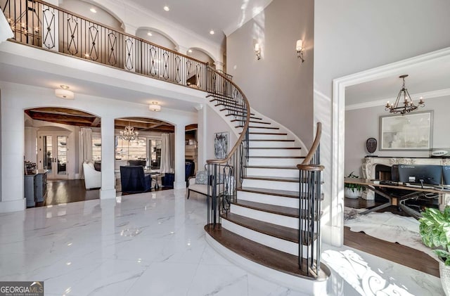 staircase featuring an inviting chandelier, ornamental molding, marble finish floor, a fireplace, and arched walkways