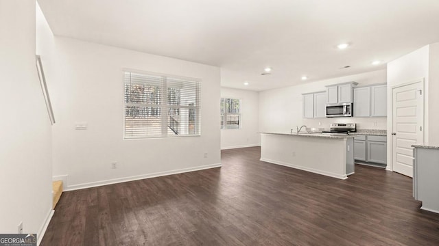 kitchen with dark wood-style floors, an island with sink, gray cabinets, and appliances with stainless steel finishes