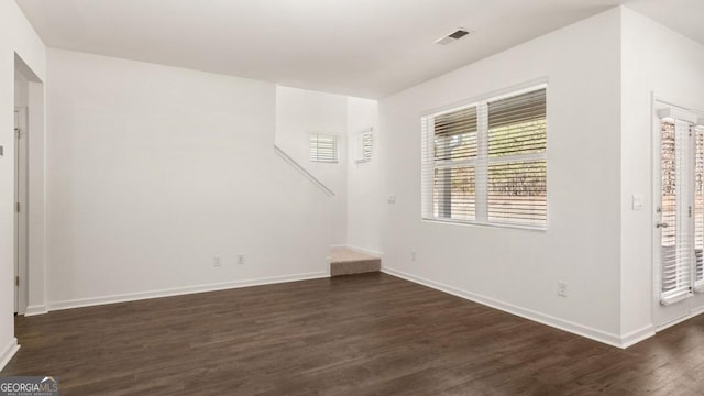 spare room with dark wood-style flooring, visible vents, and baseboards