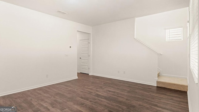 unfurnished room with dark wood-type flooring, visible vents, baseboards, and stairs