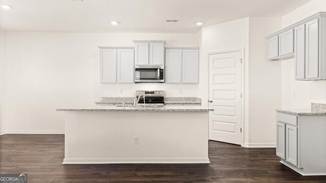 kitchen featuring appliances with stainless steel finishes, an island with sink, light stone counters, and dark wood finished floors