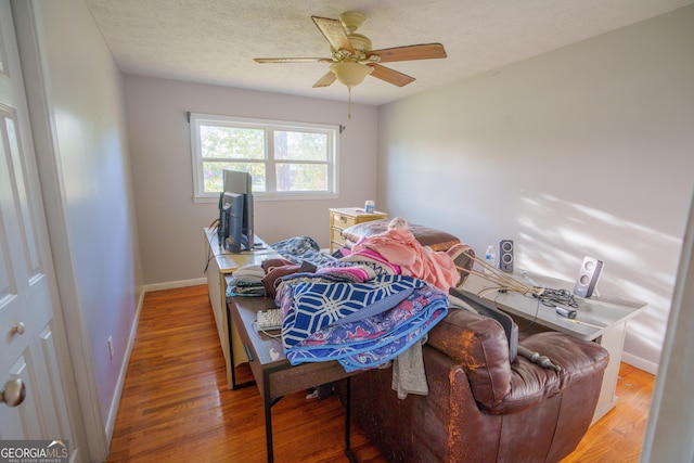 bedroom with a ceiling fan, a textured ceiling, baseboards, and light wood-type flooring