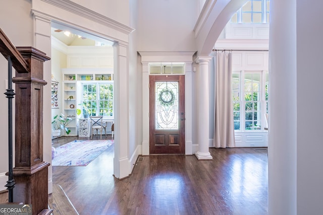entryway with arched walkways, wood finished floors, a high ceiling, and decorative columns