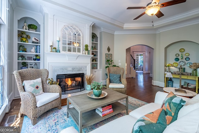 living area with arched walkways, baseboards, wood finished floors, ceiling fan, and crown molding