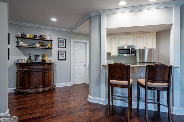 bar featuring stainless steel appliances, a dry bar, dark wood finished floors, baseboards, and ornamental molding
