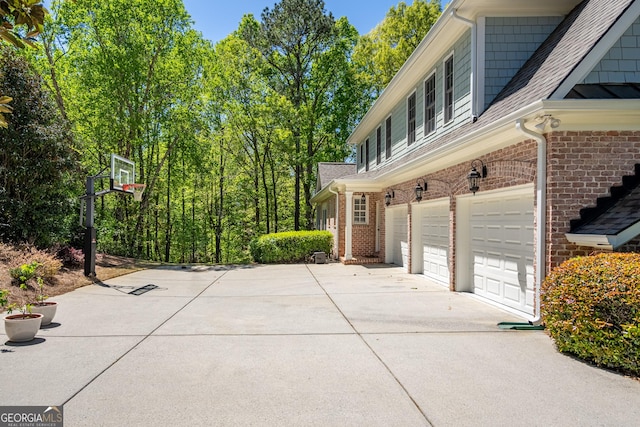 view of home's exterior with brick siding, an attached garage, concrete driveway, and roof with shingles