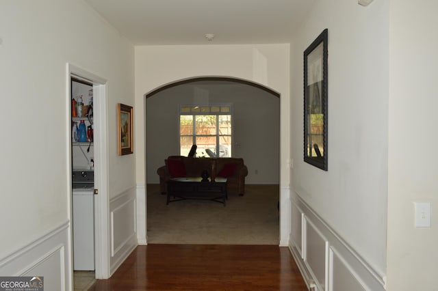 hall with a decorative wall, arched walkways, wainscoting, and dark wood-style floors
