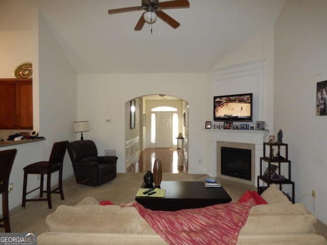 living area with a tiled fireplace, a ceiling fan, arched walkways, and lofted ceiling