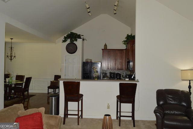kitchen featuring rail lighting, a peninsula, vaulted ceiling, black appliances, and a breakfast bar