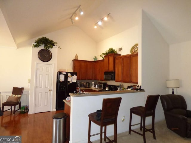 kitchen with rail lighting, a kitchen breakfast bar, a peninsula, black appliances, and brown cabinets