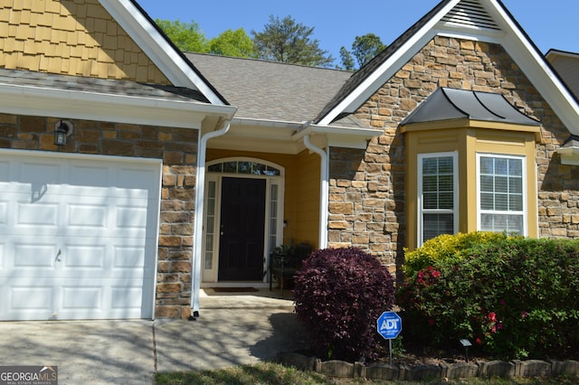 doorway to property with stone siding, a garage, and roof with shingles