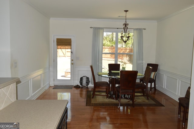 dining room with an inviting chandelier, crown molding, a wainscoted wall, a decorative wall, and wood finished floors