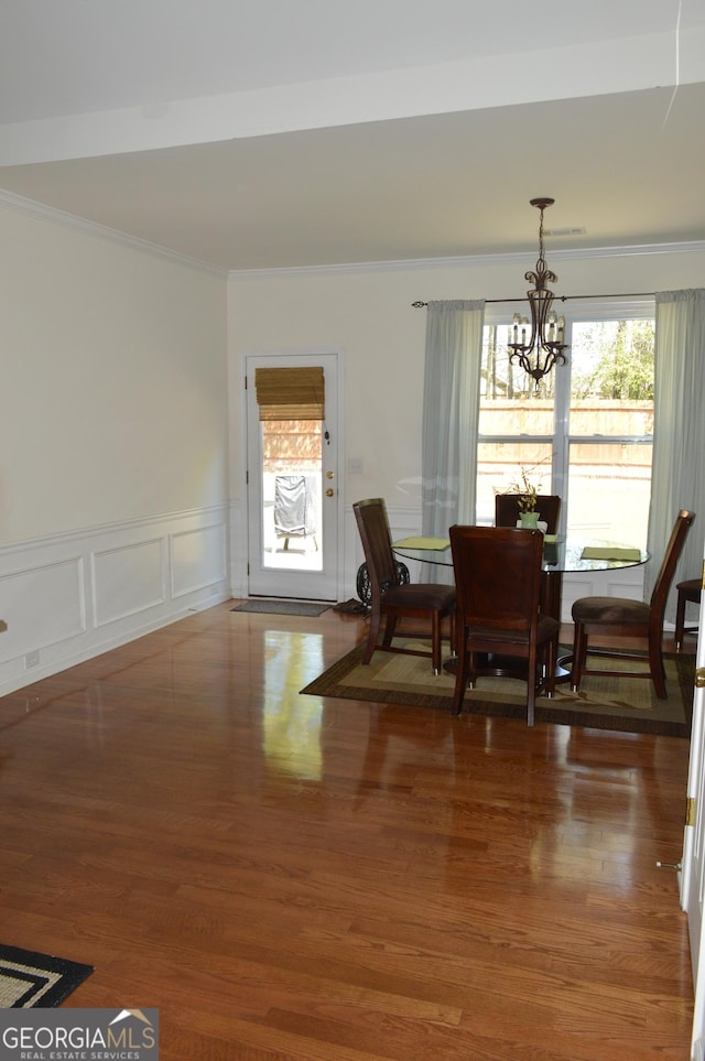 dining room featuring a wainscoted wall, an inviting chandelier, crown molding, and wood finished floors