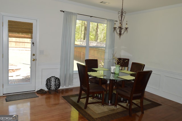dining space featuring a decorative wall, a chandelier, crown molding, wainscoting, and wood finished floors