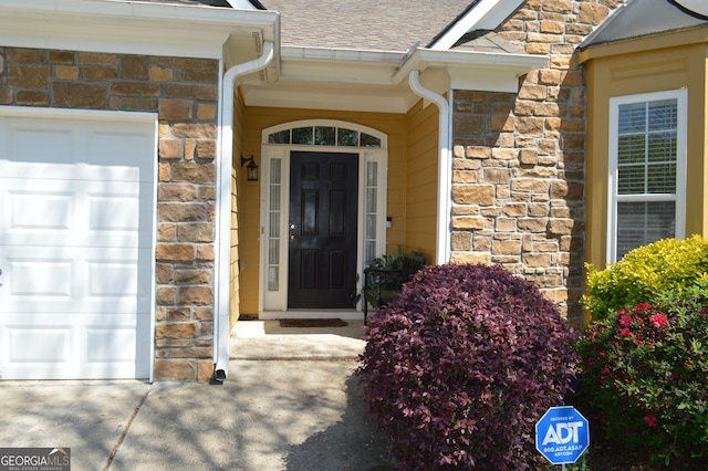 entrance to property featuring an attached garage, roof with shingles, driveway, and stone siding