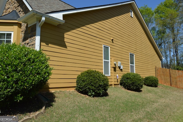 view of property exterior featuring stone siding, fence, and a lawn