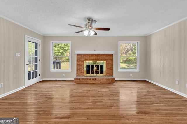 unfurnished living room featuring crown molding, hardwood / wood-style flooring, a textured ceiling, a ceiling fan, and a fireplace