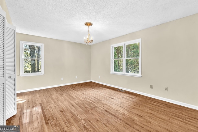 spare room featuring a chandelier, hardwood / wood-style flooring, baseboards, healthy amount of natural light, and a textured ceiling