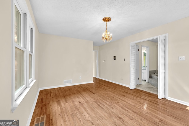 unfurnished dining area with a chandelier, light wood-style floors, baseboards, and a textured ceiling