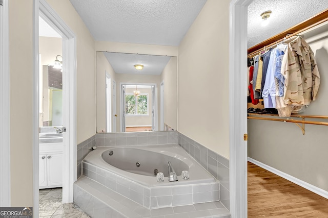 bathroom featuring a tub with jets, a spacious closet, a textured ceiling, vanity, and baseboards