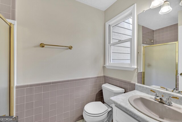 full bathroom with a shower stall, tile walls, a wainscoted wall, toilet, and vanity