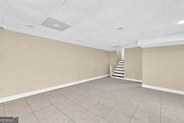 finished below grade area featuring a drop ceiling, stairs, baseboards, and light tile patterned flooring