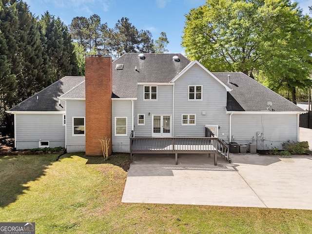 rear view of house featuring a patio, a wooden deck, a lawn, a chimney, and roof with shingles