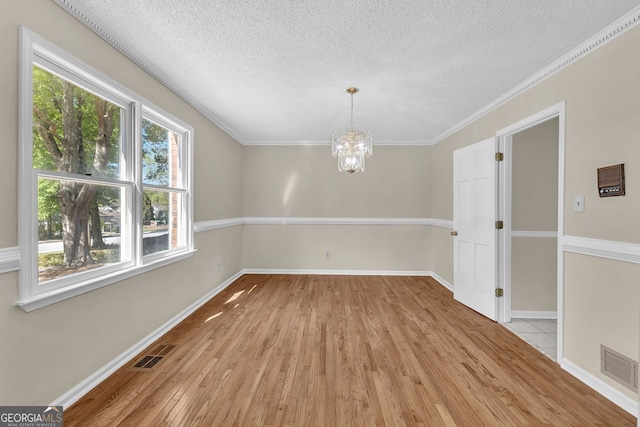 unfurnished dining area featuring plenty of natural light, light wood-type flooring, a textured ceiling, a chandelier, and baseboards