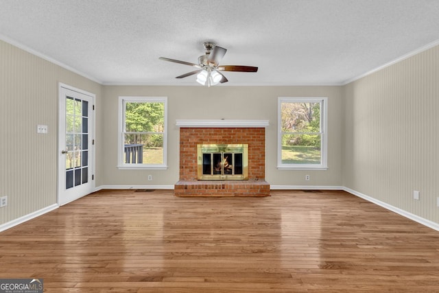 unfurnished living room featuring hardwood / wood-style floors, ornamental molding, a textured ceiling, a ceiling fan, and a fireplace