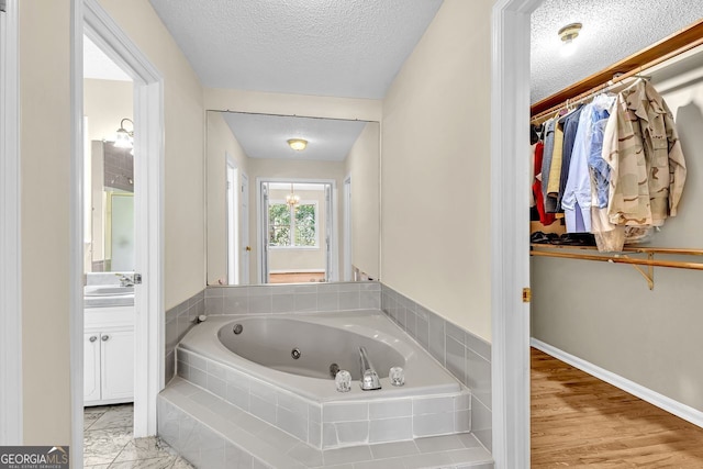 full bath with a walk in closet, a tub with jets, vanity, and a textured ceiling