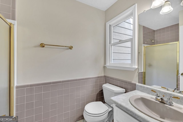 bathroom with a stall shower, tile walls, toilet, a wainscoted wall, and vanity