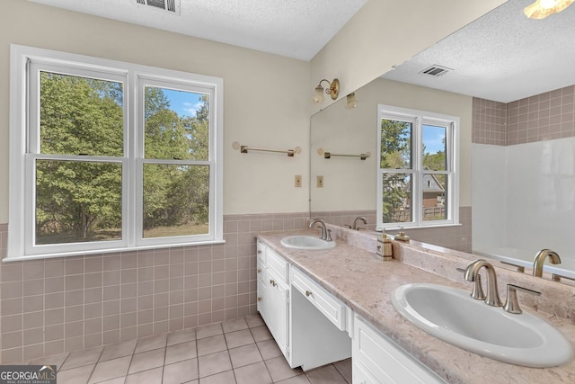 bathroom with tile walls, tile patterned floors, healthy amount of natural light, a textured ceiling, and wainscoting