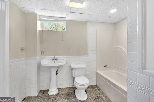 bathroom with toilet, tile walls, shower / tub combination, a paneled ceiling, and wainscoting