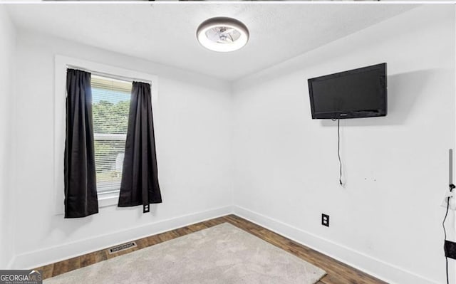 empty room with dark wood-type flooring, visible vents, and baseboards
