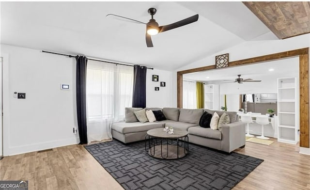 living area with a ceiling fan, baseboards, vaulted ceiling, and light wood-type flooring