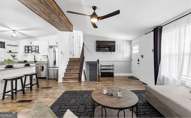 living room with vaulted ceiling with beams, wood finished floors, ceiling fan, and stairway