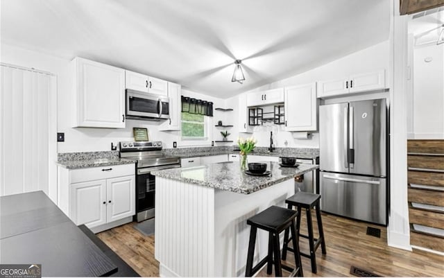 kitchen featuring vaulted ceiling, a kitchen bar, stainless steel appliances, white cabinets, and dark wood-type flooring