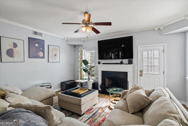 living room with visible vents, wood finished floors, ceiling fan, a fireplace, and ornamental molding