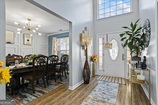 entryway featuring crown molding, wood finished floors, an inviting chandelier, baseboards, and visible vents